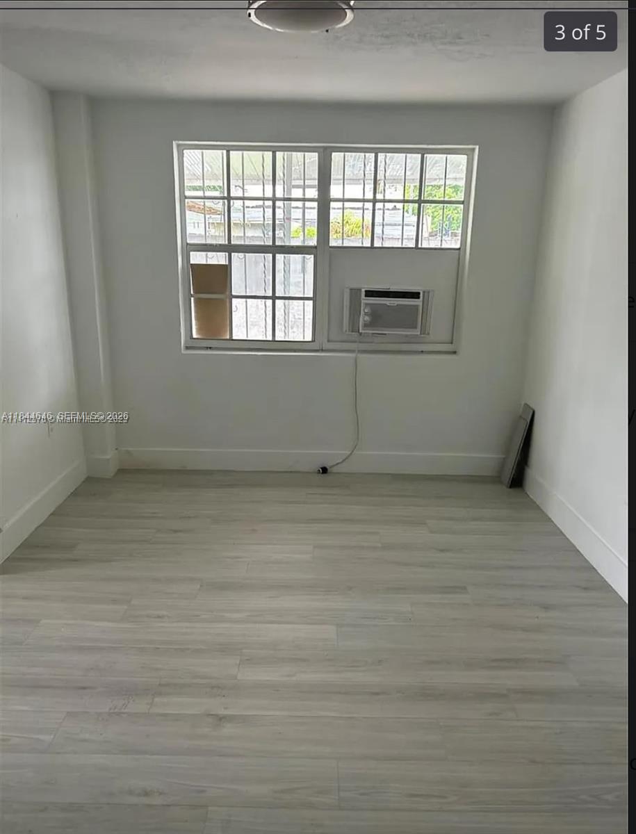An empty room features light-colored wood-look flooring, white walls, and a window with an AC unit — 2215 NW 33rd St, Miami FL 33142, MIAMI, FL