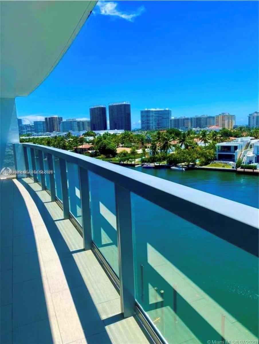 A balcony with a glass railing overlooks a canal, palm trees, and distant high-rise buildings — 9261 E Bay Harbor Dr # 704, Bay Harbor Islands FL 33154, BAY HARBOR ISLANDS, FL
