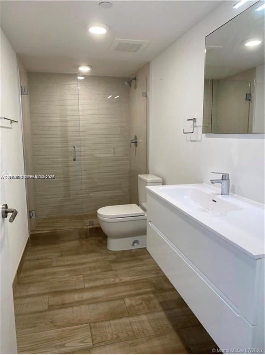 A modern bathroom features a glass-enclosed shower, a white vanity, and wood-look tile flooring — 9261 E Bay Harbor Dr # 704, Bay Harbor Islands FL 33154, BAY HARBOR ISLANDS, FL