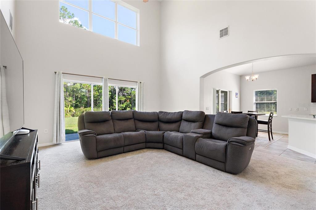 A spacious living room features a large gray sectional sofa, high ceilings, and sliding doors — 4039 NAVIGATOR WAY, KISSIMMEE, FL