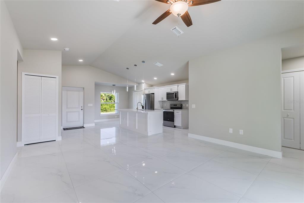 A bright, open-concept kitchen and living area features white cabinetry, a center island, and glossy tile flooring — 1962 LEGHORN STREET, LEHIGH ACRES, FL