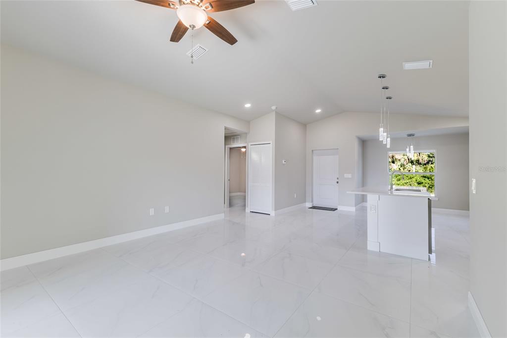 An open-concept living area features white marble-look tile flooring, a ceiling fan, and a kitchen — 1962 LEGHORN STREET, LEHIGH ACRES, FL