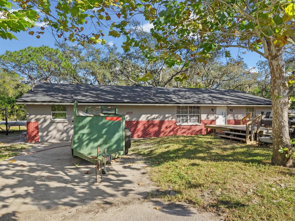 A single-story house with a brick and siding exterior features a green trailer in front — 12218 ELKTON AVENUE, HUDSON, FL