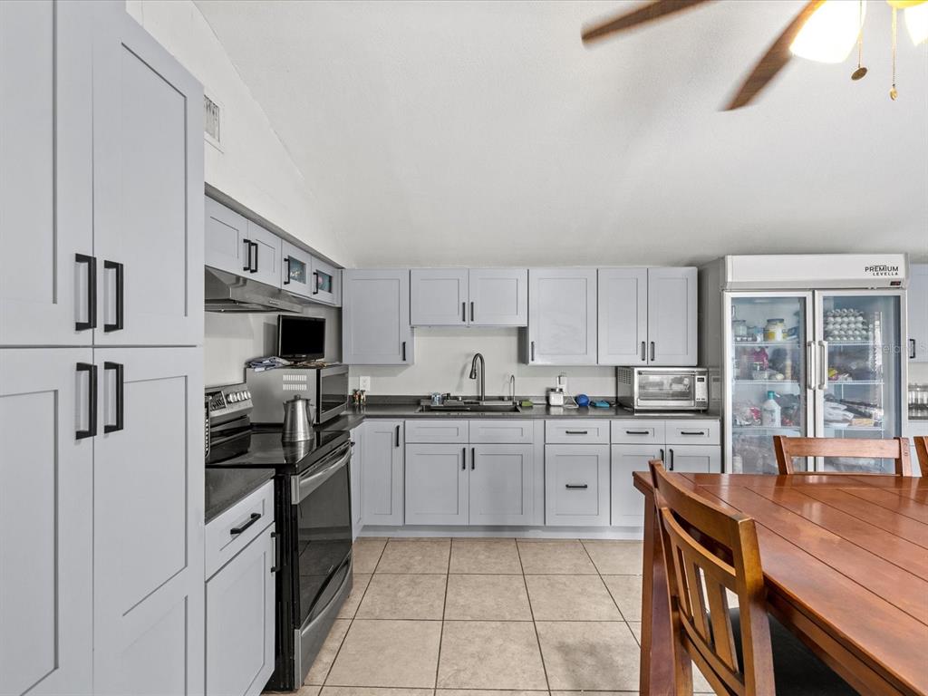 A kitchen features light gray cabinets, black countertops, stainless steel appliances, and tile flooring — 12218 ELKTON AVENUE, HUDSON, FL
