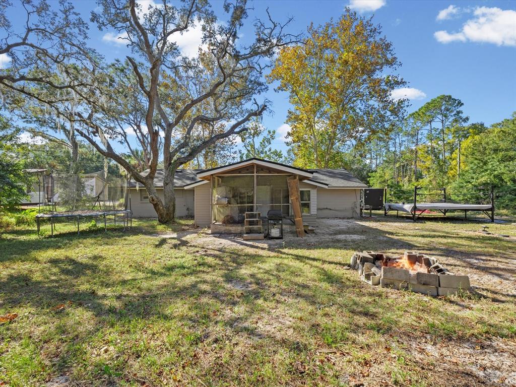 A backyard view of a house with a screened porch, fire pit, and wrestling ring — 12218 ELKTON AVENUE, HUDSON, FL