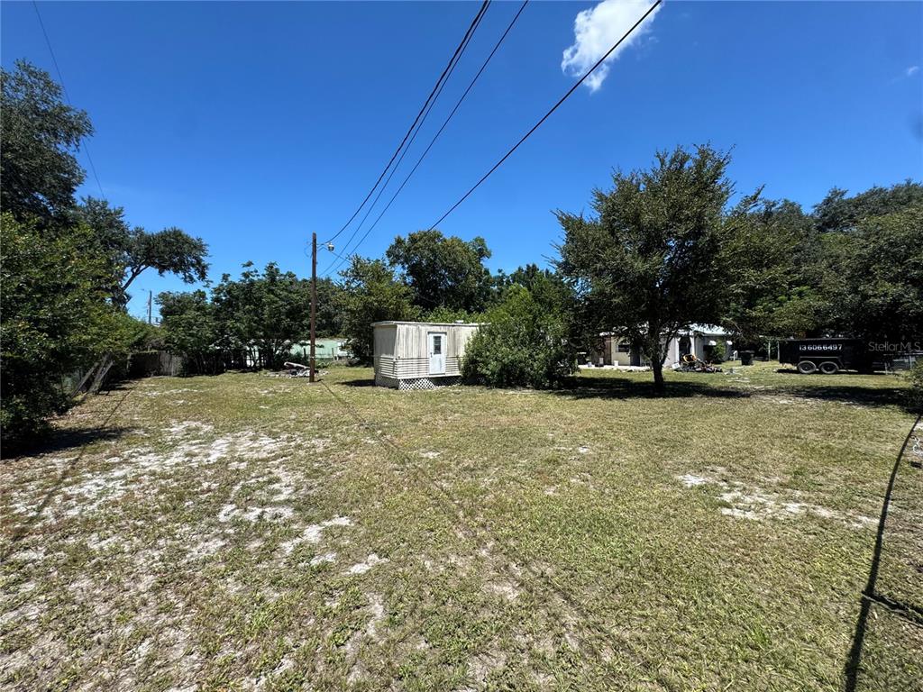 A grassy lot features a small, light-colored shed and mature trees under a blue sky — 2795 JANIE LANE, BARTOW, FL