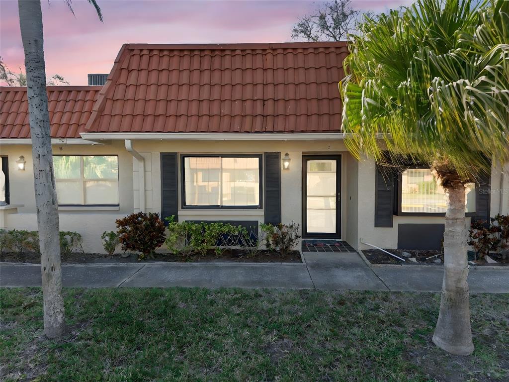 A single-story townhouse exterior features a red tile roof, beige stucco walls, and dark shutters — 19029 US HIGHWAY 19 N UNIT 18F, CLEARWATER, FL