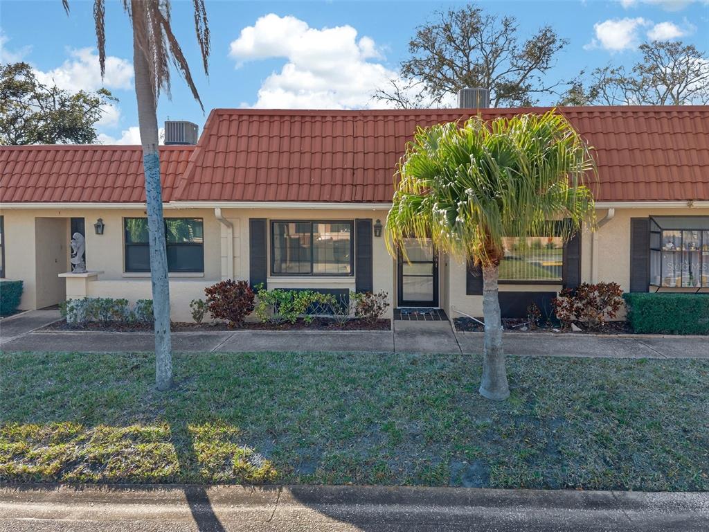 A single-story townhouse with a red tile roof, beige stucco walls, and two palm trees — 19029 US HIGHWAY 19 N UNIT 18F, CLEARWATER, FL