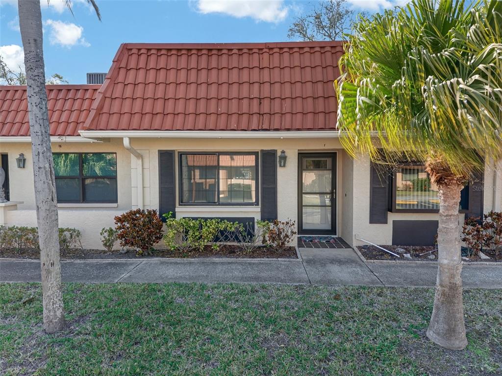 A single-story residential unit features a red tile roof, beige stucco walls, and black shutters — 19029 US HIGHWAY 19 N UNIT 18F, CLEARWATER, FL