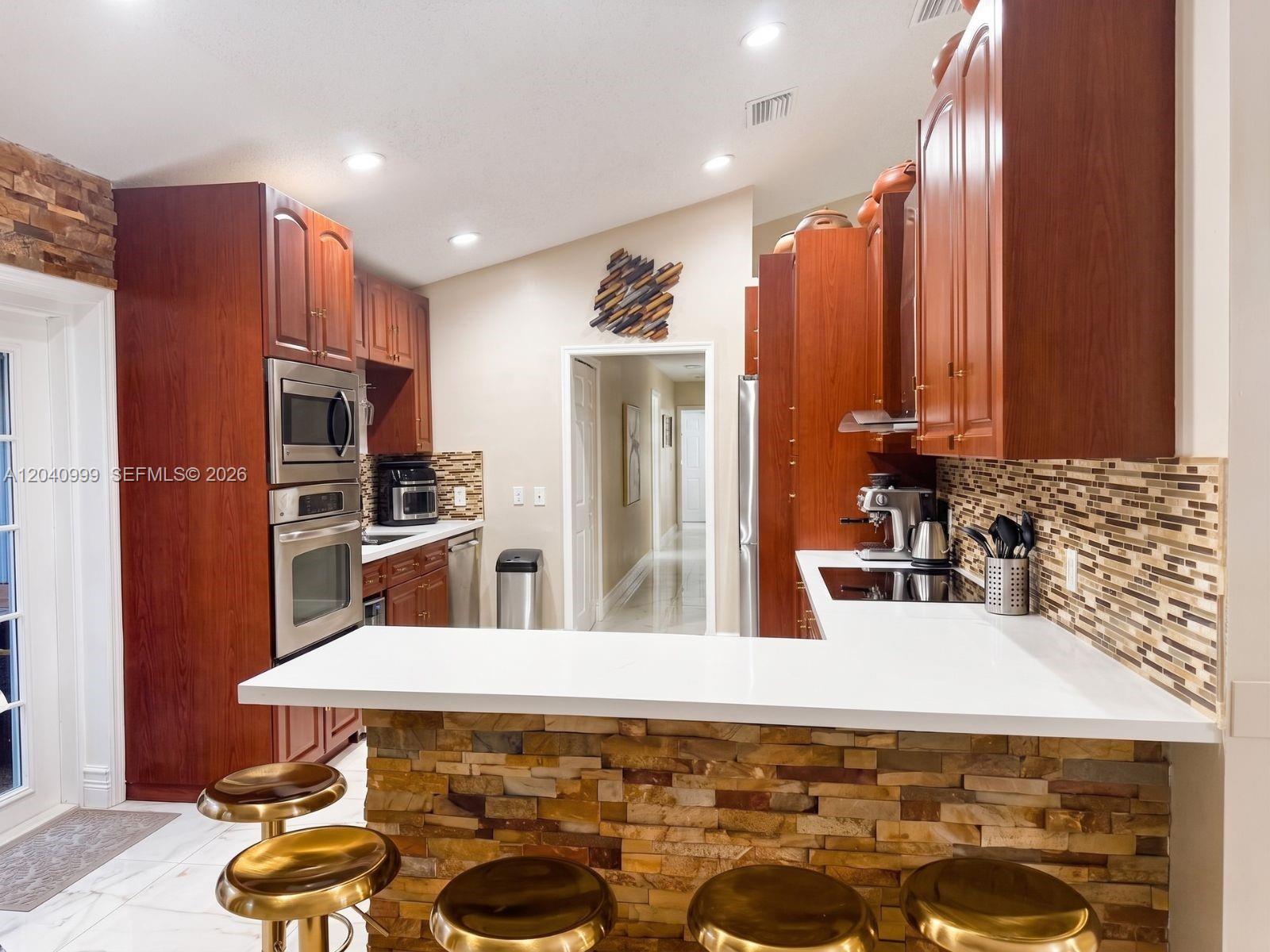 A kitchen features cherry wood cabinets, a stone-faced breakfast bar, and white countertops — 324 Patio Village Ter, Weston FL 33326, WESTON, FL