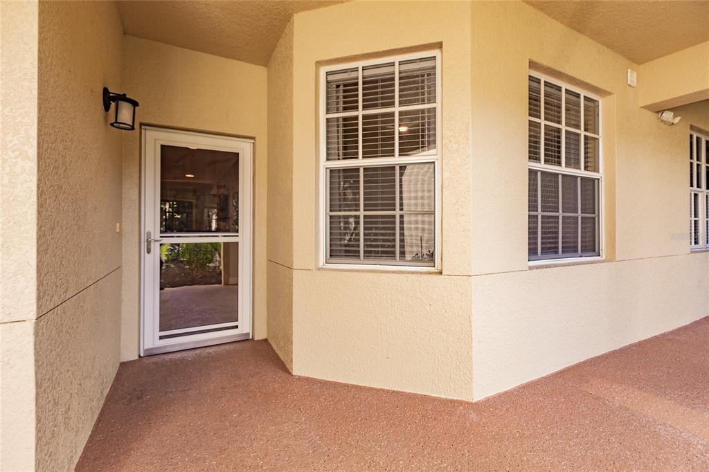 A beige stucco exterior features a glass storm door and two windows on a patio — 1878 TARPON BAY DRIVE S UNIT 102, NAPLES, FL