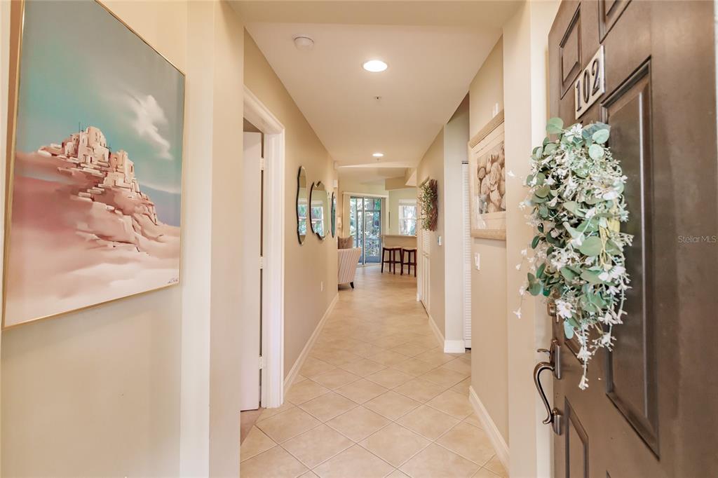 A tiled hallway leads from an entryway door toward a sunlit living area — 1878 TARPON BAY DRIVE S UNIT 102, NAPLES, FL