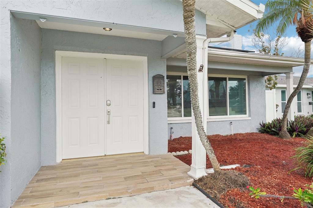 A light blue house exterior features a double front door and a tiled porch area — 6010 BAYOU GRANDE BOULEVARD NE, ST PETERSBURG, FL