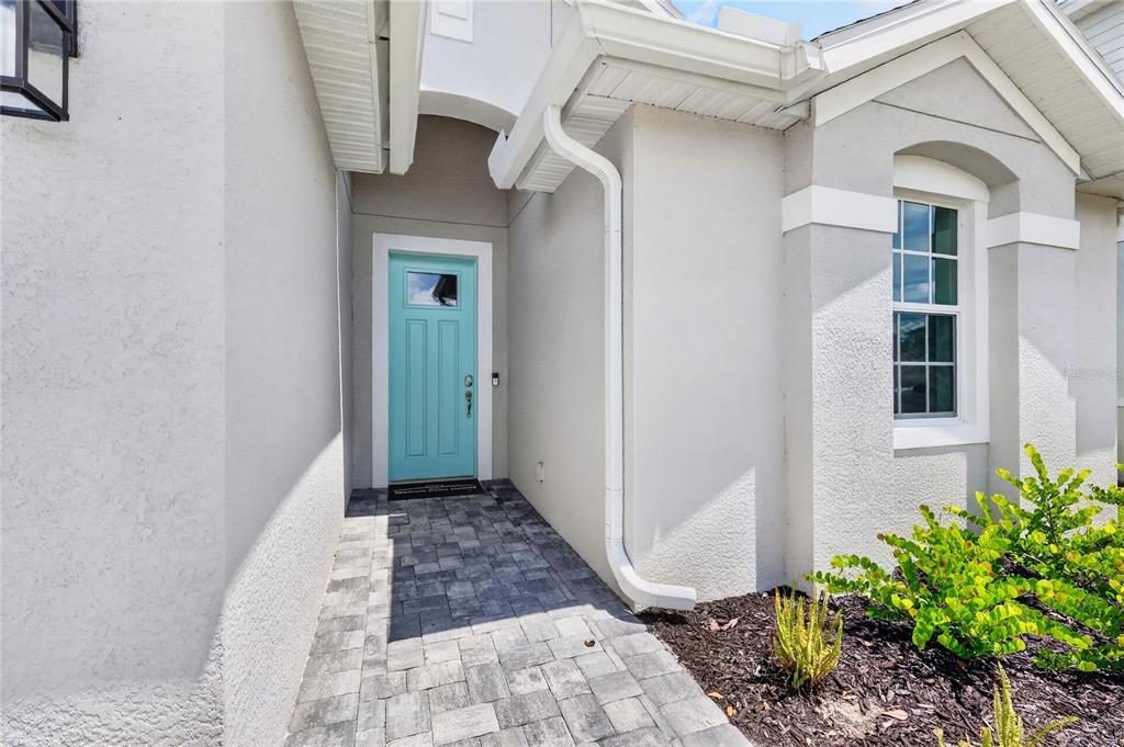 A light blue front door is set within a covered entryway with gray paver flooring — 15766 ELINA SKY DRIVE, PUNTA GORDA, FL
