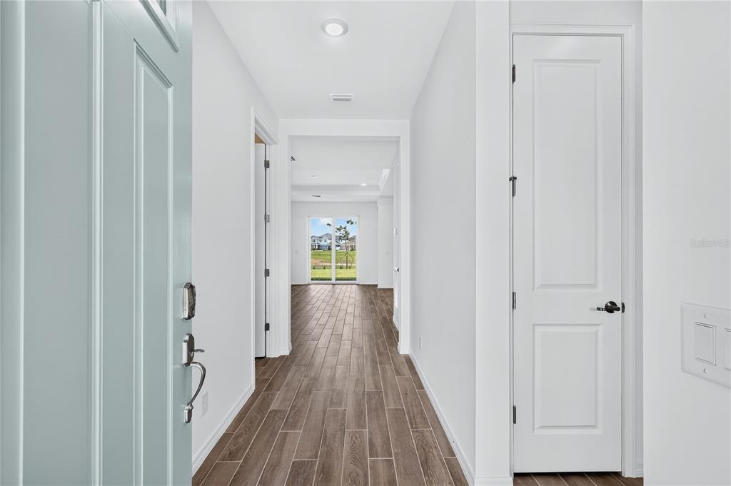 A bright entryway with wood-look tile flooring leads to a hallway with a glass door — 15766 ELINA SKY DRIVE, PUNTA GORDA, FL