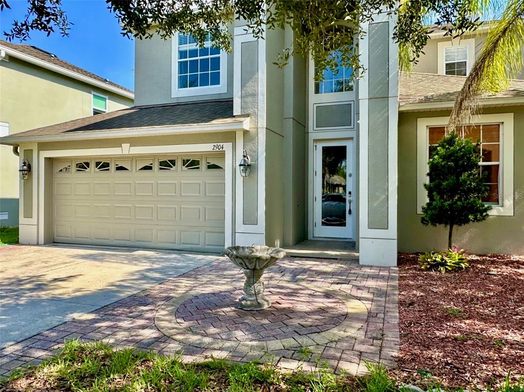 A two-story house exterior features a garage, a paved walkway, and a stone birdbath — 2904 TRINITY COTTAGE DRIVE, LAND O LAKES, FL