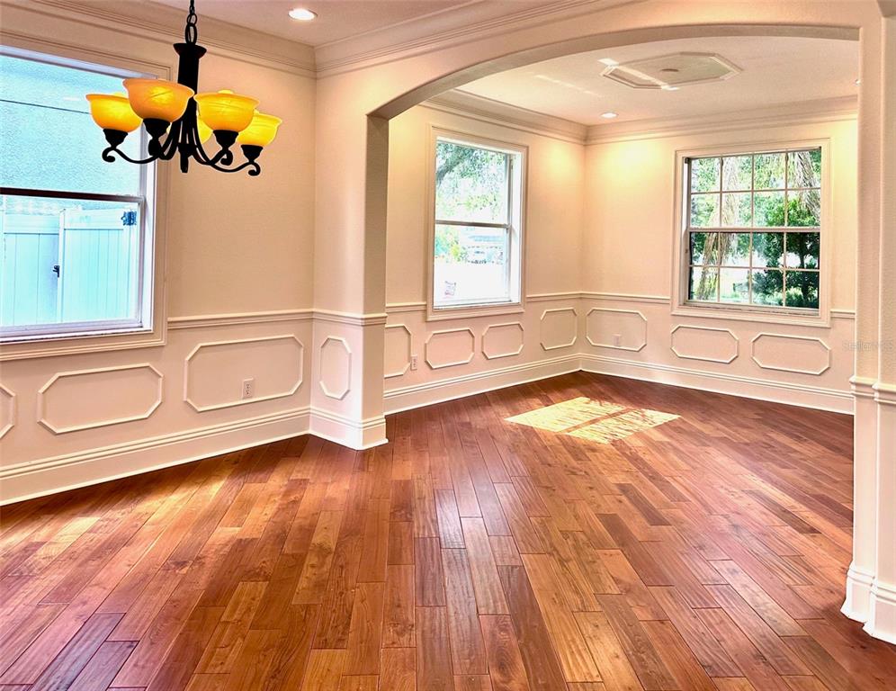 A dining room with hardwood floors, wainscoting, and a chandelier, opening into an adjacent room — 2904 TRINITY COTTAGE DRIVE, LAND O LAKES, FL
