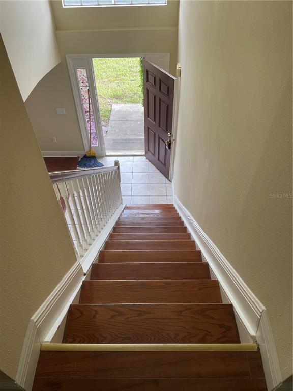 A view looking down a wooden staircase toward an open front door and tiled entryway — 5064 SPANISH OAKS BOULEVARD, LAKELAND, FL