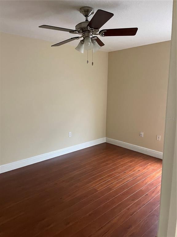 An empty room features beige walls, dark wood-look flooring, and a ceiling fan — 5064 SPANISH OAKS BOULEVARD, LAKELAND, FL