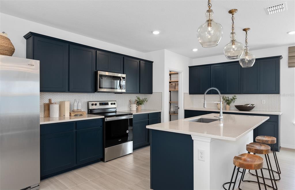 A modern kitchen features dark blue cabinets, stainless steel appliances, and a central island — 5093 STARLING BIRD LANE, ST CLOUD, FL