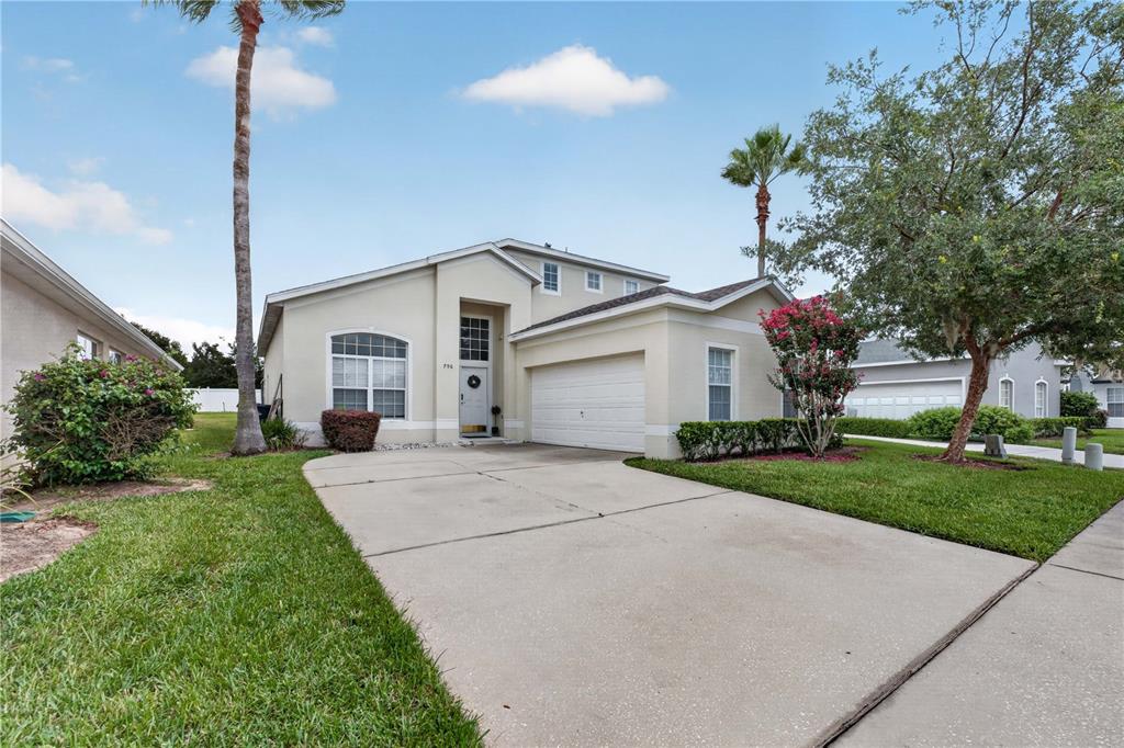 A beige, two-story suburban house with a concrete driveway, a garage, and palm trees — 706 LOCKBREEZE DRIVE, DAVENPORT, FL