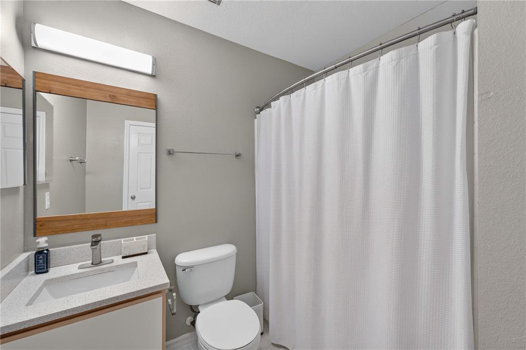 A bathroom features a wood-framed mirror, a white vanity, a toilet, and a white shower curtain — 706 LOCKBREEZE DRIVE, DAVENPORT, FL