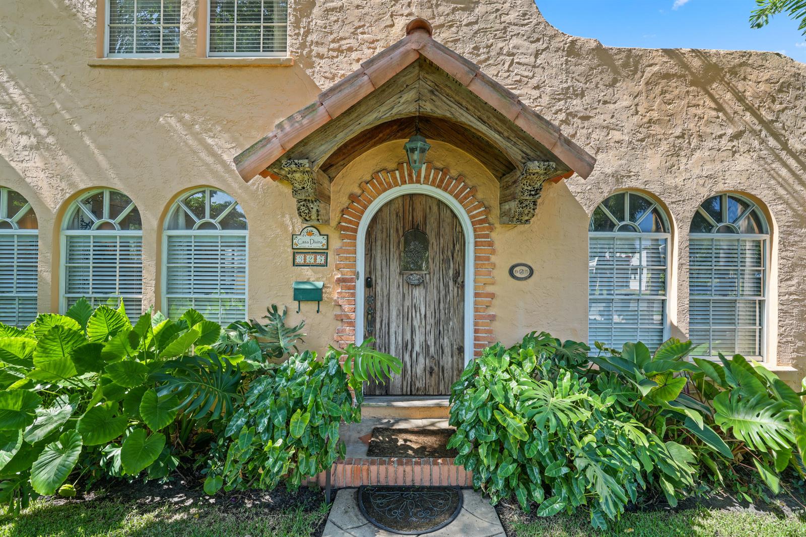 The exterior of a stucco home features an arched wooden door under a tiled canopy — 325 Greymon Drive, West Palm Beach FL 33405, WEST PALM BEACH, FL