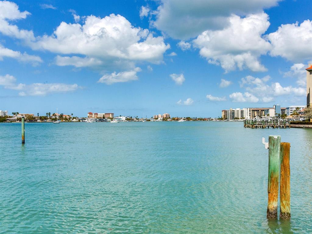 A view of a calm bay with distant buildings and wooden pilings in the foreground — 210 DOLPHIN POINT UNIT B, CLEARWATER BEACH, FL