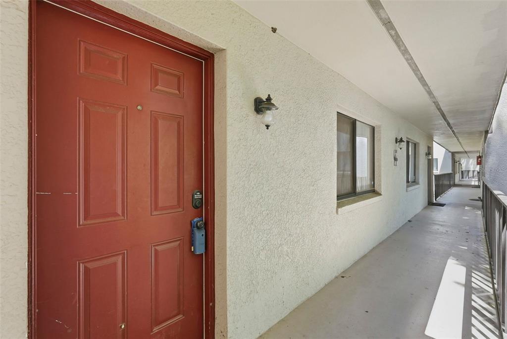 A red front door opens onto an outdoor concrete walkway of a multi-story apartment building — 11709 RAINTREE VILLAGE BOULEVARD UNIT C, TEMPLE TERRACE, FL