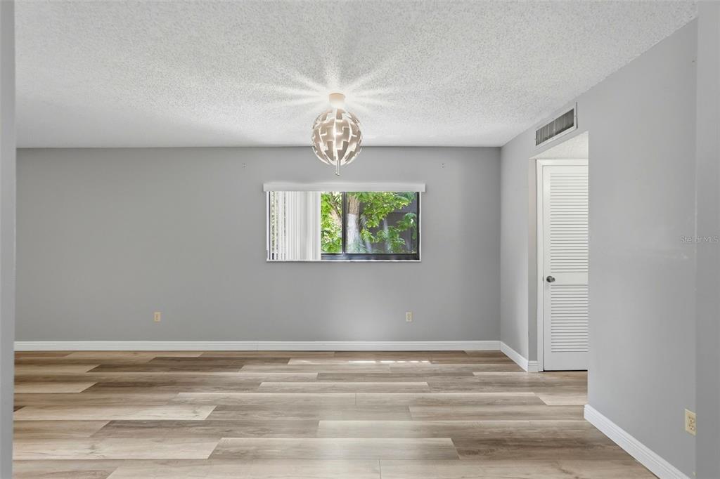 An empty room with gray walls, wood-look flooring, a central light fixture, and a window — 11709 RAINTREE VILLAGE BOULEVARD UNIT C, TEMPLE TERRACE, FL