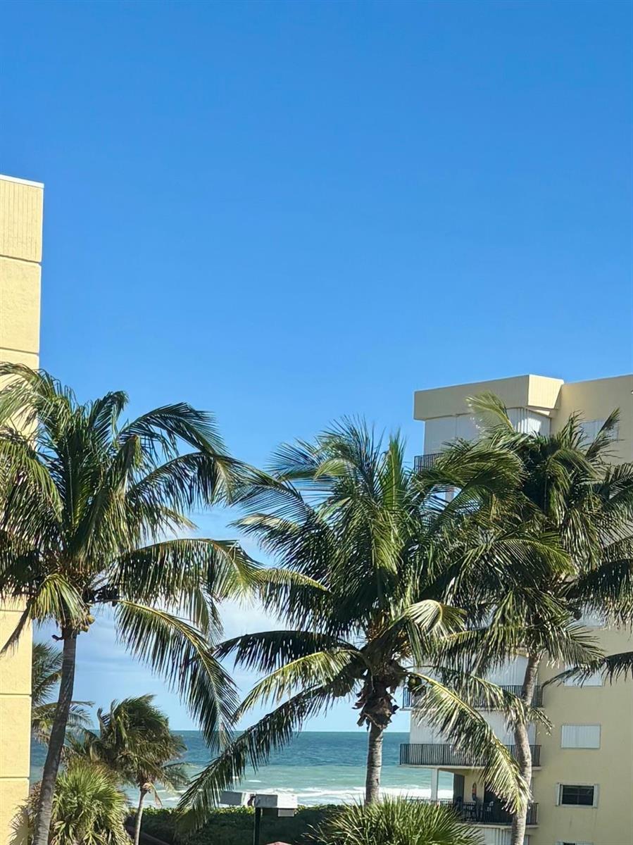 A view of the ocean framed by palm trees between two yellow apartment buildings — 126 Ocean Bay Drive # 126, Jensen Beach FL 34957, JENSEN BEACH, FL
