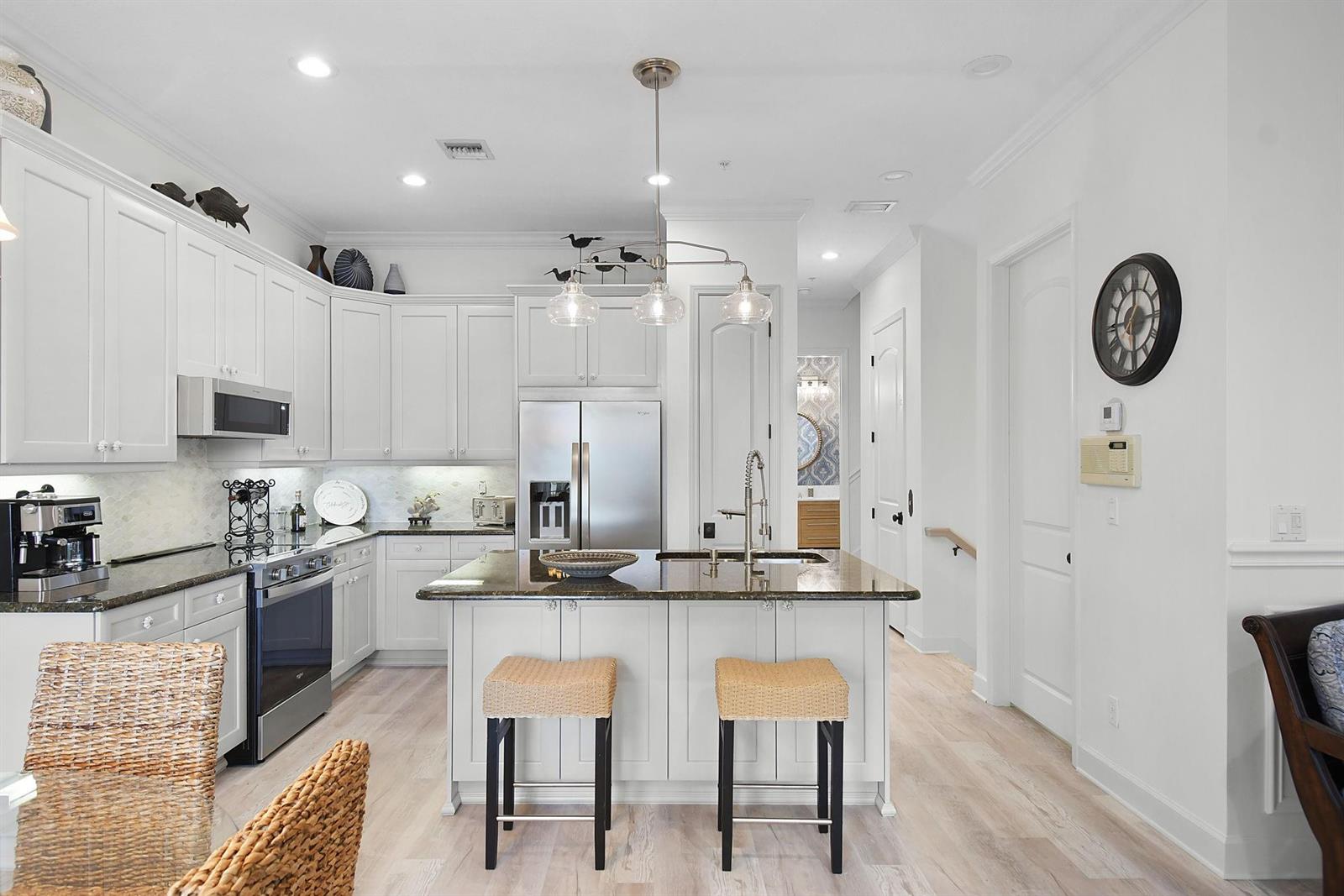 A white kitchen features a central island with two stools and stainless steel appliances — 126 Ocean Bay Drive # 126, Jensen Beach FL 34957, JENSEN BEACH, FL