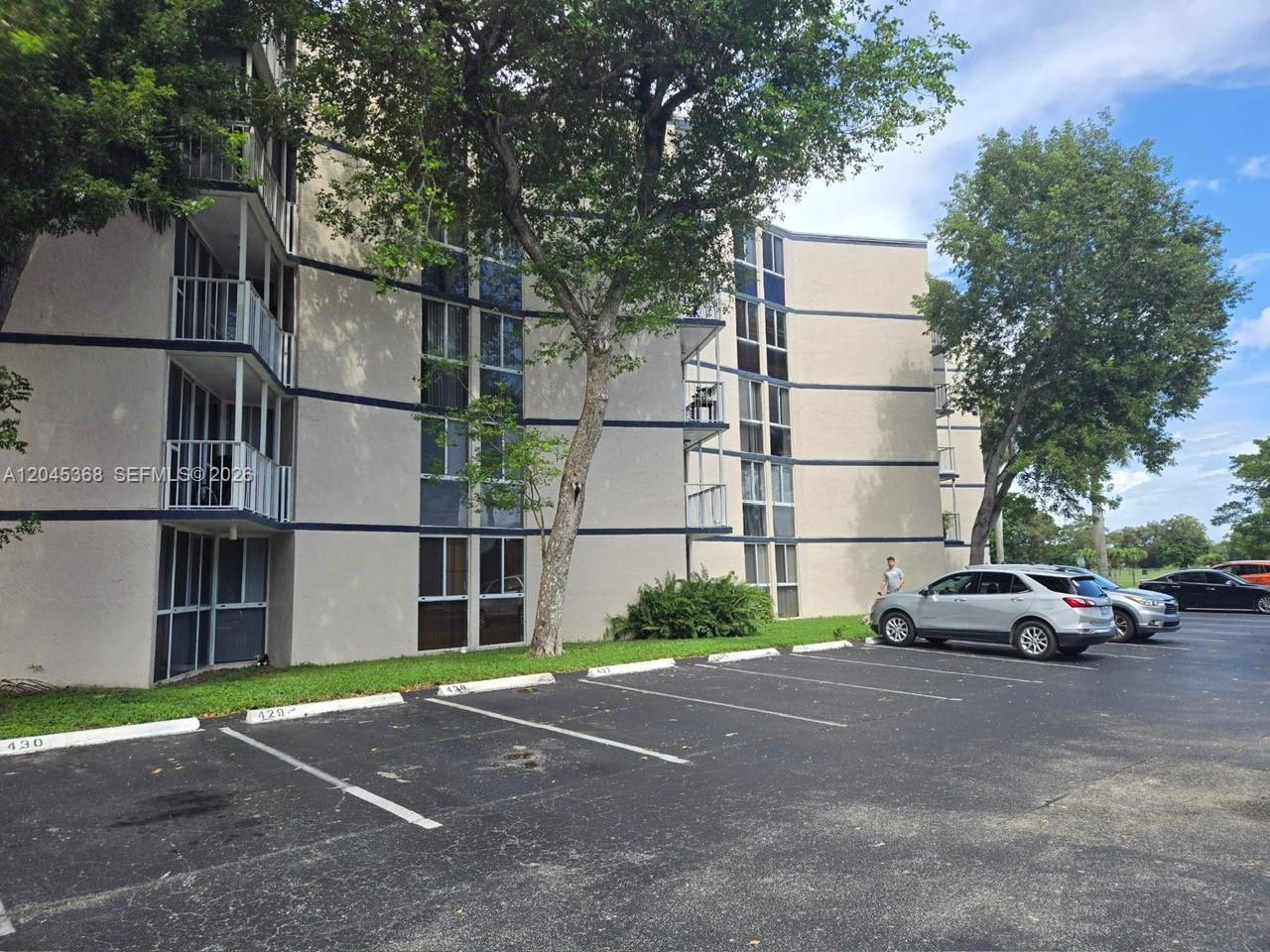 A multi-story apartment building with balconies stands beside a parking lot with several cars — 6995 NW 186th St # E403, Hialeah FL 33015, HIALEAH, FL