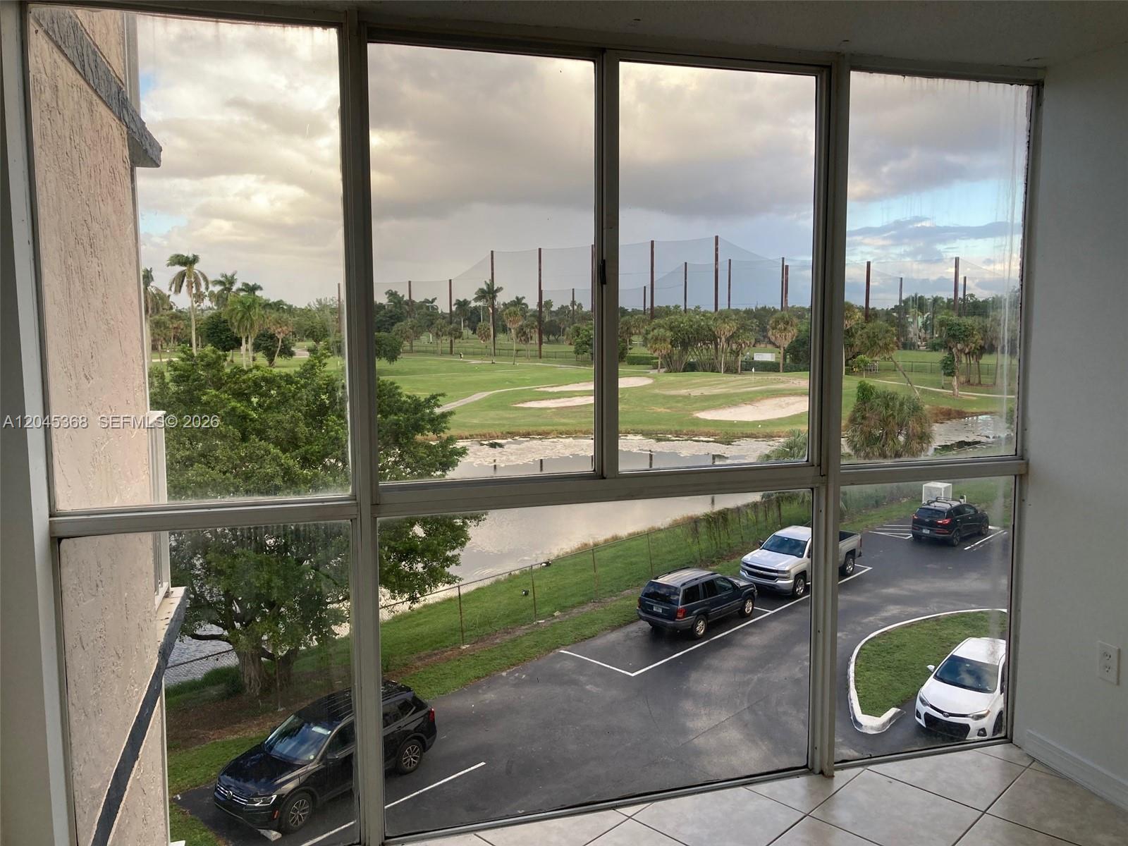 A view from a window overlooking a parking lot, a pond, and a golf course — 6995 NW 186th St # E403, Hialeah FL 33015, HIALEAH, FL