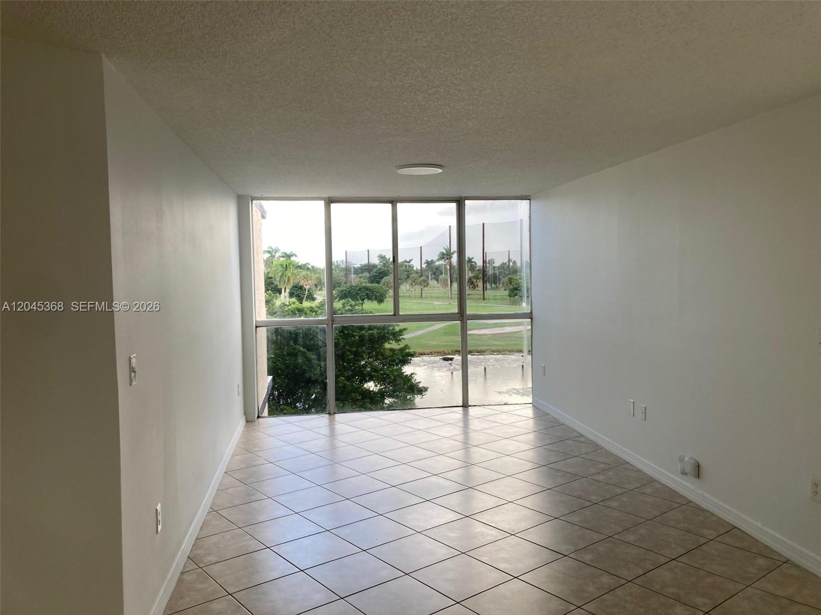 An empty room with tiled floors and large windows overlooking a golf course and pond — 6995 NW 186th St # E403, Hialeah FL 33015, HIALEAH, FL