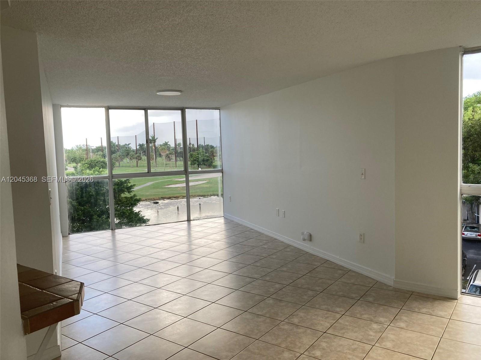 An empty room with tiled floors and large windows overlooking a golf course and pond — 6995 NW 186th St # E403, Hialeah FL 33015, HIALEAH, FL