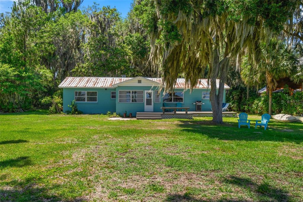 A teal single-story house with a metal roof sits on a grassy lawn under trees — 12525 NE 204TH TERRACE, WALDO, FL