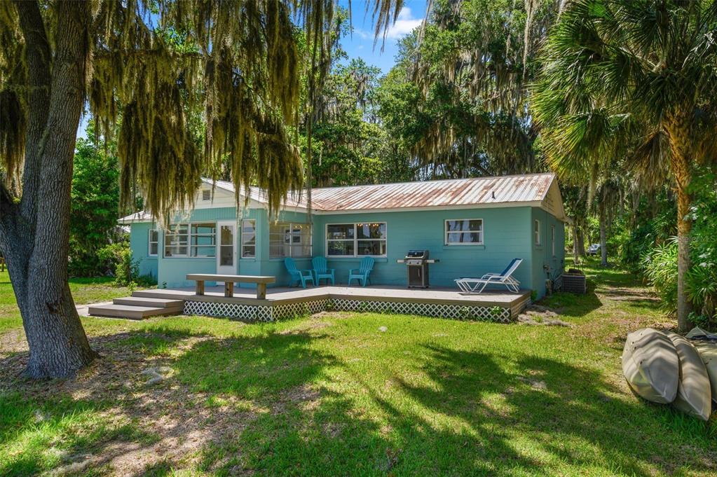 A teal house with a metal roof and a wooden deck sits among mossy trees — 12525 NE 204TH TERRACE, WALDO, FL