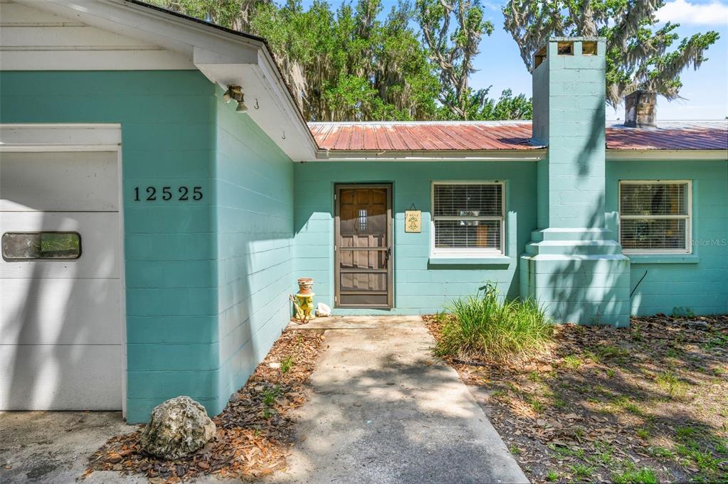 A teal-colored house exterior features a concrete walkway, a front door, and a brick chimney — 12525 NE 204TH TERRACE, WALDO, FL
