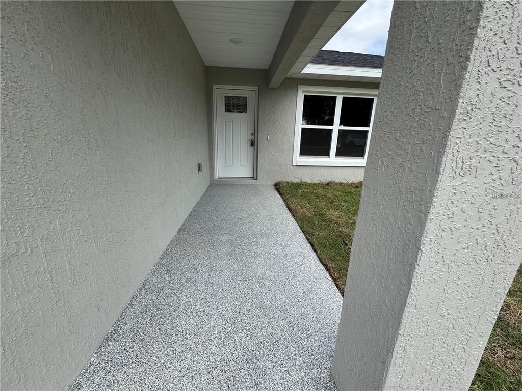 A covered entryway features a gray textured floor, a white front door, and stucco walls — 3941 SE 137TH LANE, SUMMERFIELD, FL