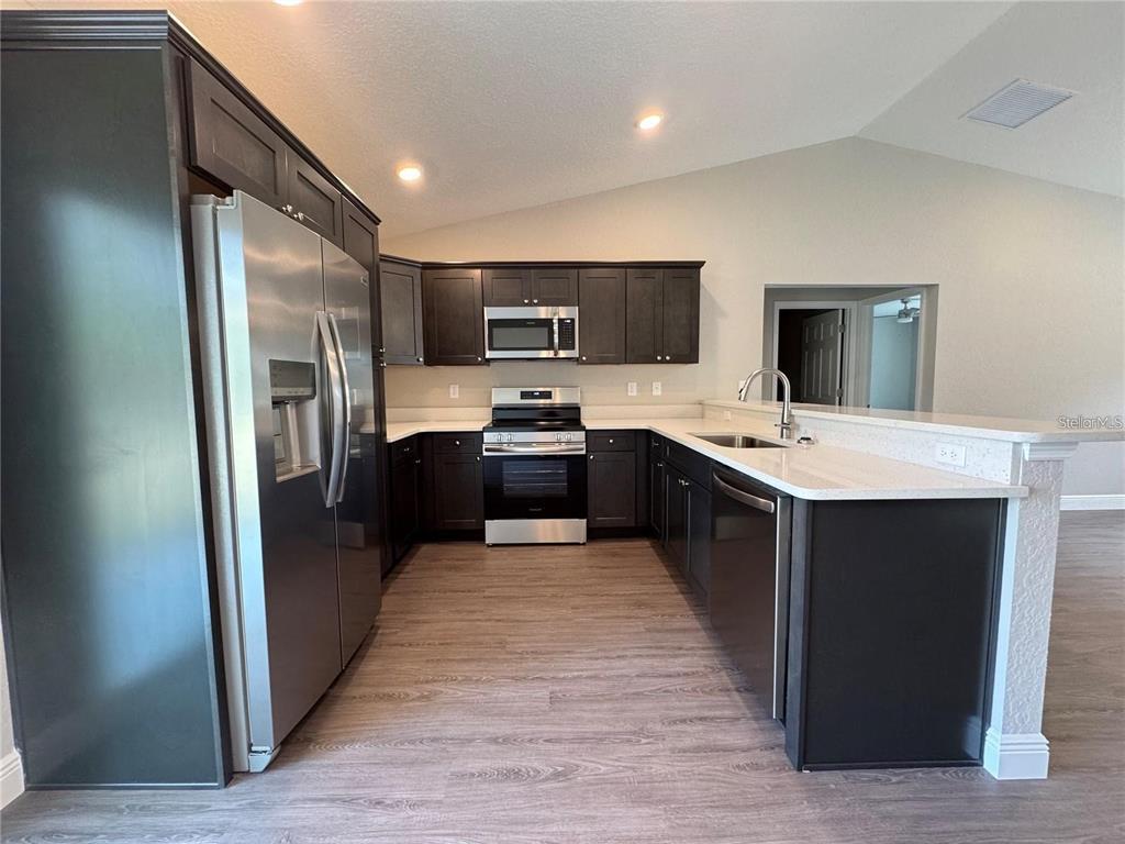 A kitchen features dark wood cabinets, stainless steel appliances, and white countertops — 3941 SE 137TH LANE, SUMMERFIELD, FL