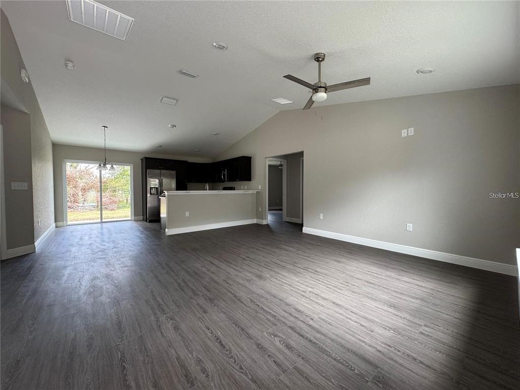 An open-concept living area features gray wood-look flooring, a ceiling fan, and a kitchen — 3941 SE 137TH LANE, SUMMERFIELD, FL