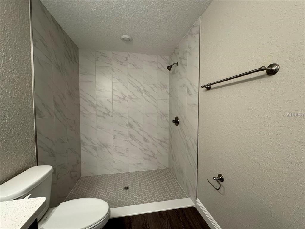 A bathroom features a walk-in shower with marble-look tile walls and a gray hexagonal floor — 3941 SE 137TH LANE, SUMMERFIELD, FL