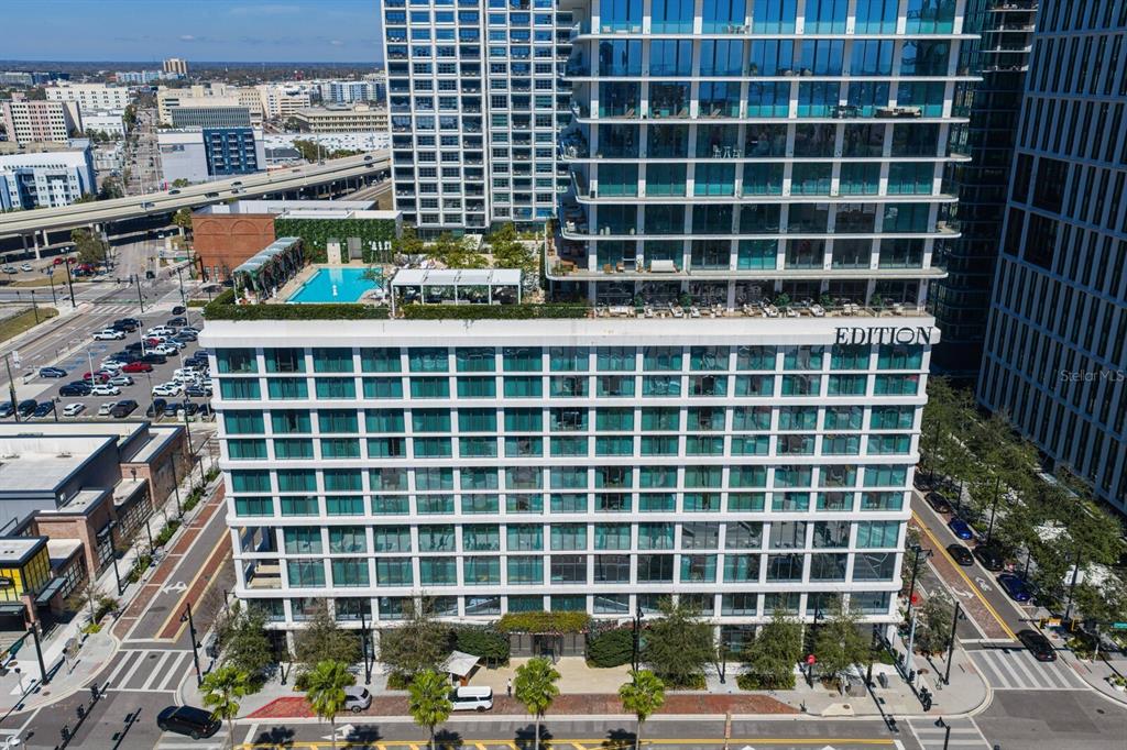 An aerial view shows the exterior of a modern high-rise building with a rooftop pool — 1000 WATER STREET UNIT 1502, TAMPA, FL