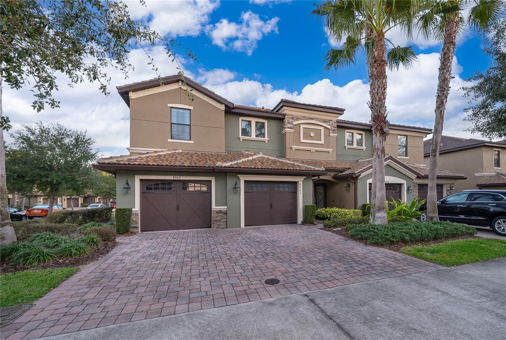 A two-story house with a brick paver driveway, two garage doors, and palm trees — 8945 AZALEA SANDS LANE UNIT 8945, CHAMPIONS GATE, FL