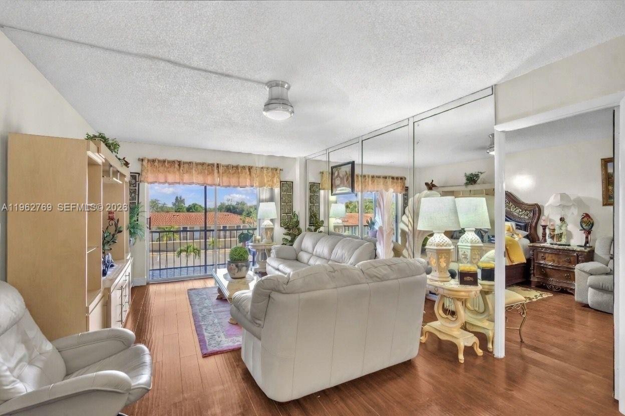 A living room with wood flooring, mirrored walls, a white sofa, and a balcony view — 4160 Inverrary Dr # 308, Lauderhill FL 33319, LAUDERHILL, FL