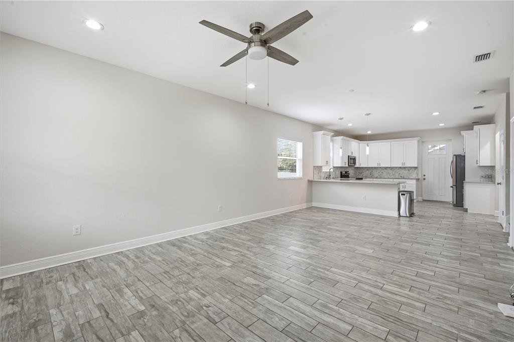 An open-concept living area features gray wood-look tile flooring, a ceiling fan, and a kitchen — 2904 BANZA STREET, TAMPA, FL