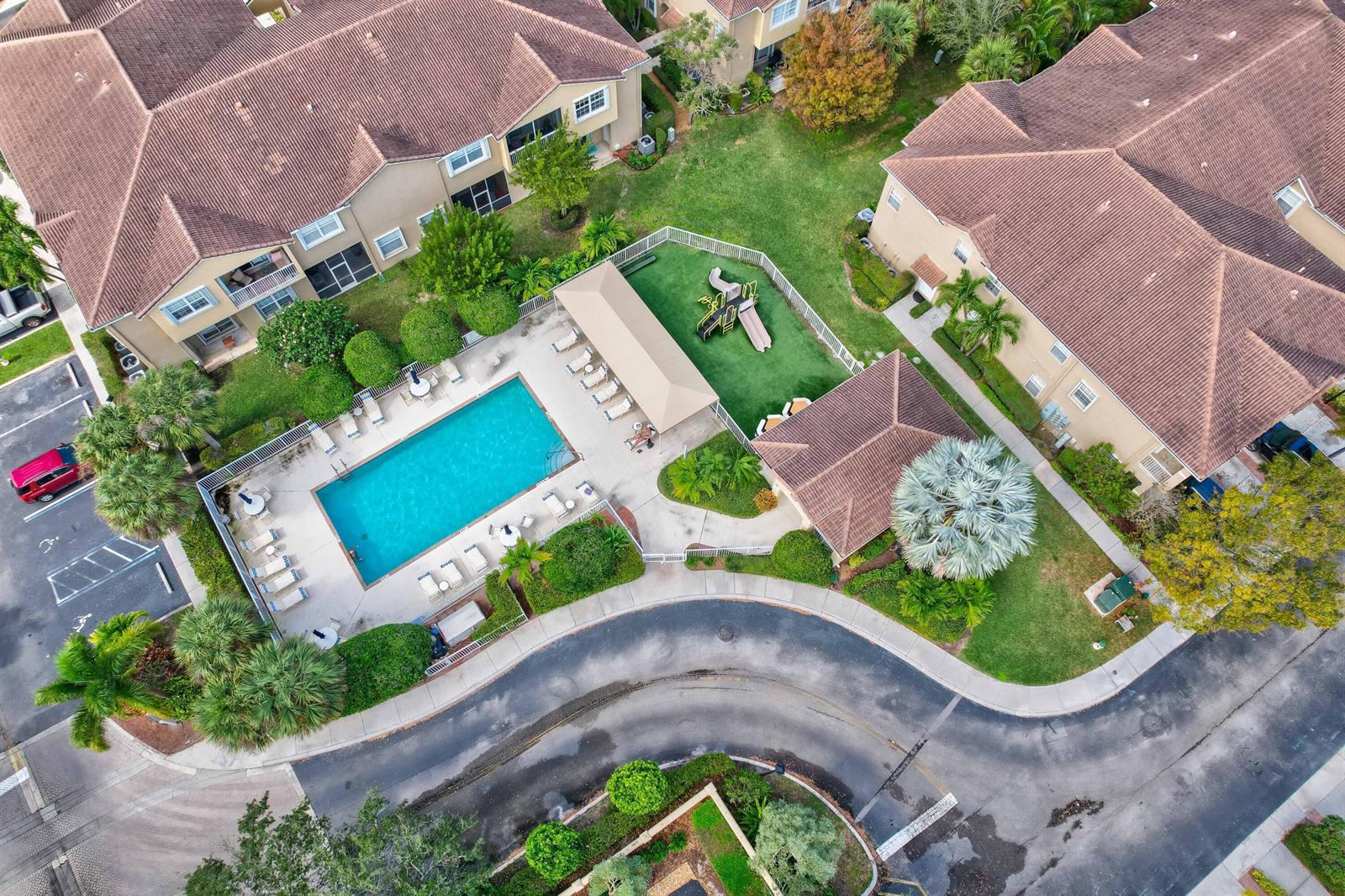 An aerial view shows a community swimming pool, playground, and clubhouse surrounded by apartment buildings — 115 Lighthouse Circle # B, Tequesta FL 33469, TEQUESTA, FL