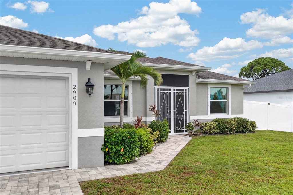 A gray single-story house features a white garage door, a paved walkway, and landscaping — 2909 NW 24TH AVENUE, CAPE CORAL, FL