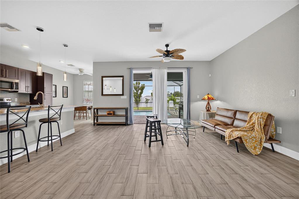 A living room with wood-look tile floors, a brown sofa, and a sliding door to a pool — 2909 NW 24TH AVENUE, CAPE CORAL, FL